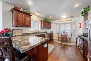 Kitchen featuring visible vents, dark wood-style flooring, a peninsula, stainless steel appliances, and a kitchen bar