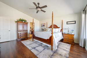 Bedroom featuring dark wood-style floors, baseboards, vaulted ceiling, and ensuite bathroom