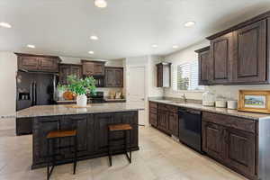 Kitchen featuring dark brown cabinetry, black appliances, a kitchen breakfast bar, and a center island