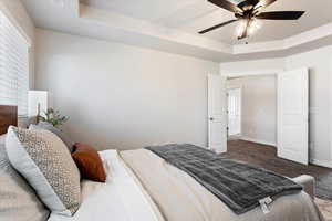 Bedroom with a ceiling fan, baseboards, a tray ceiling, and carpet flooring