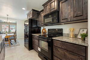 Kitchen featuring light stone counters, dark brown cabinetry, and black appliances