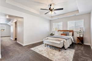 Bedroom with baseboards, visible vents, a tray ceiling, and dark colored carpet