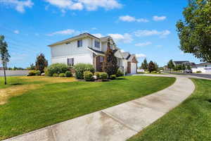 View of front facade featuring concrete driveway, fence, a front lawn, board and batten siding, and brick siding