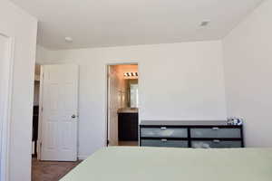 Carpeted bedroom with visible vents, connected bathroom, and a sink