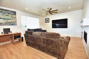 Living area with light wood finished floors, a fireplace, a ceiling fan, and recessed lighting