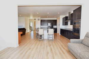 Kitchen with a breakfast bar, open floor plan, appliances with stainless steel finishes, wall chimney range hood, and light wood finished floors