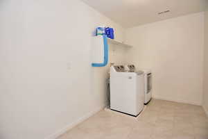 Clothes washing area featuring light tile patterned floors, visible vents, washer and dryer, laundry area, and baseboards