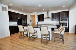 Kitchen with light wood-style flooring, a sink, black fridge with ice dispenser, visible vents, and wall chimney range hood