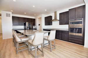 Kitchen with visible vents, appliances with stainless steel finishes, a kitchen breakfast bar, wall chimney range hood, and a sink