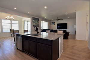 Kitchen featuring an island with sink, light wood-style flooring, open floor plan, stainless steel dishwasher, and a sink