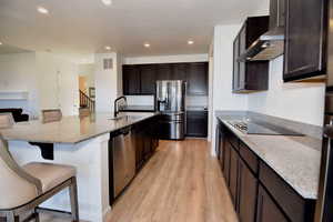 Kitchen featuring visible vents, wall chimney exhaust hood, appliances with stainless steel finishes, a kitchen bar, and a sink