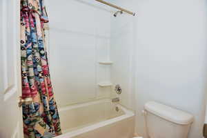 Full bathroom featuring shower / bathtub combination with curtain and toilet
