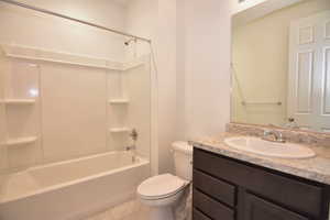 Bathroom with toilet, tile patterned flooring, washtub / shower combination, and vanity