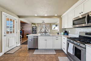 Kitchen featuring white cabinets, appliances with stainless steel finishes, a peninsula, and a sink