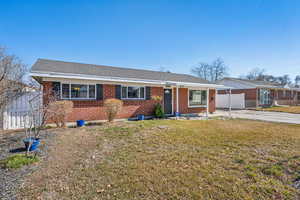 Ranch-style house featuring a shingled roof, brick siding, fence, concrete driveway, and a front lawn