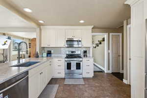 Kitchen with light stone counters, a sink, white cabinetry, and appliances with stainless steel finishes