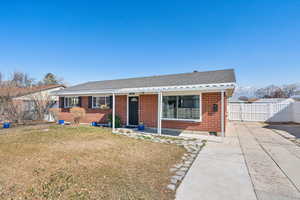 View of front of property with brick siding, fence, roof with shingles, a gate, and a front yard