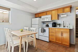 Kitchen featuring white appliances, brown cabinets, light countertops, a sink, and light tile patterned flooring