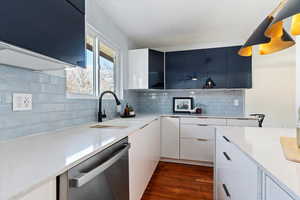 Kitchen with dark wood-style flooring, light countertops, decorative backsplash, stainless steel dishwasher, and a sink