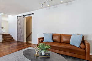 Living room with a barn door, wood finished floors, baseboards, stairway, and rail lighting