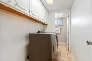 Laundry area with cabinet space, washer and clothes dryer, baseboards, and light tile patterned flooring