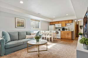 Living room featuring a tray ceiling, light tile patterned floors, recessed lighting, light colored carpet, and stairs