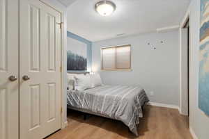 Bedroom with a textured ceiling, wood finished floors, visible vents, and baseboards