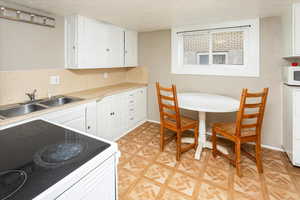 Kitchen featuring range with electric cooktop, white cabinets, white microwave, a textured ceiling, and a sink