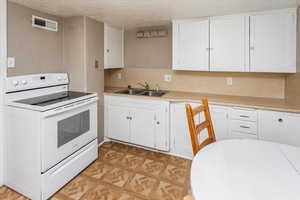 Kitchen with white electric range oven, visible vents, white cabinetry, a sink, and a textured ceiling