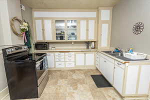 Kitchen featuring a sink, visible vents, light countertops, stainless steel electric stove, and glass insert cabinets