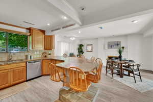 Kitchen with stainless steel dishwasher, healthy amount of natural light, beam ceiling, light wood-type flooring, and ornamental molding