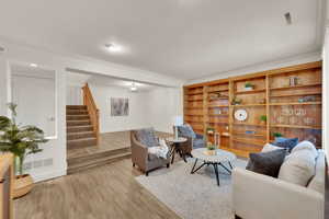 Living room featuring stairway, light wood-type flooring, and crown molding