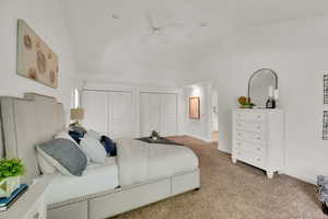 Carpeted bedroom with two closets, vaulted ceiling, and a ceiling fan