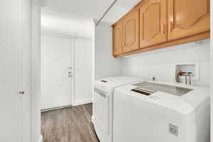 Laundry room with cabinet space, light wood-type flooring, and washing machine and clothes dryer