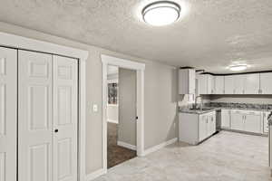 Kitchen with dishwasher, light stone counters, a sink, and white cabinets