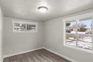 Empty room with baseboards, dark carpet, and a textured ceiling