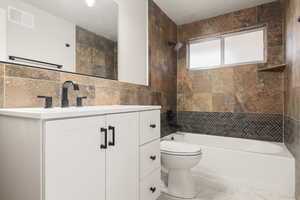 Full bathroom featuring shower / bath combination, visible vents, toilet, vanity, and tile walls