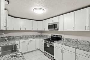 Kitchen with marble finish floor, stainless steel appliances, a sink, and white cabinets