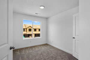 Unfurnished room with visible vents, carpet flooring, a textured ceiling, and baseboards