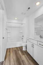 Full bath featuring toilet, wood finished floors, vanity, visible vents, and shower / washtub combination