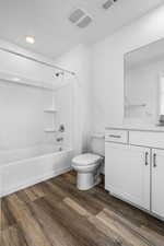 Bathroom featuring bathtub / shower combination, visible vents, toilet, vanity, and wood finished floors