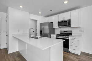 Kitchen featuring stainless steel appliances, visible vents, a sink, and dark wood-type flooring