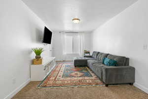 Living area featuring baseboards, a textured ceiling, and light colored carpet