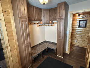 Mudroom with a textured ceiling, dark wood-type flooring, log walls, and baseboards