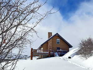 Snow covered back of property with a deck and a chimney