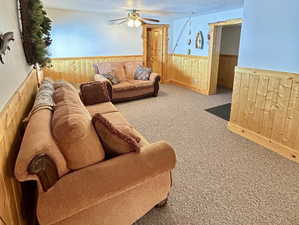 Carpeted living room featuring a wainscoted wall, ceiling fan, wooden walls, and a textured ceiling