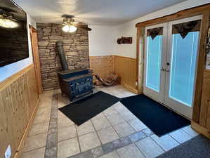 Doorway featuring a ceiling fan, wainscoting, a wood stove, french doors, and wood walls