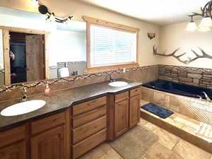 Bathroom with a garden tub, double vanity, a sink, and stone tile flooring