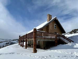 Snow covered property with stairs, a chimney, and a deck