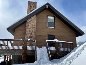 Snow covered back of property with stone siding, a chimney, and a deck